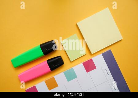 Top view flat lay composition with colorful markers and sticky notes arranged near planner calendar on yellow background Stock Photo