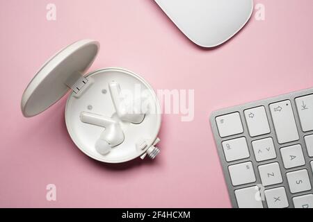 Top view composition of white true wireless earbuds in case placed near laptop keyboard and mouse on pink desk Stock Photo