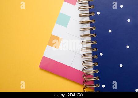 Top view composition with multicolored planner calendar and blue spiral notebook stacked on yellow background Stock Photo