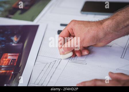 Crop unrecognizable male architect creating draft of building and erasing lines while working on project at home Stock Photo