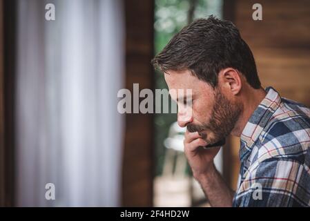 Concentrated male architect with blueprint speaking on mobile phone while working at home and discussing new project Stock Photo