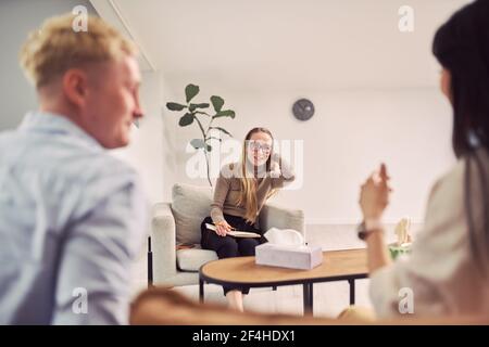 Multiethnic couple sitting on couch and talking about mental problems during therapy session with psychologist Stock Photo