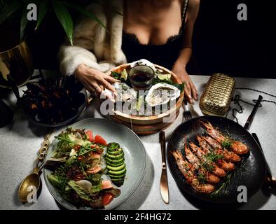 Woman in expensive dress in seafood restaurant eating oysters prawns mussels and avocado salad Stock Photo
