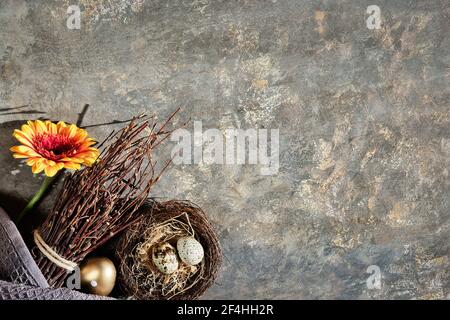 Easter decorations with copy-space, place for text. Orange red gerbera flower, quail eggs in nest, bunch of twigs, natural homemade decor. Seasonal ar Stock Photo