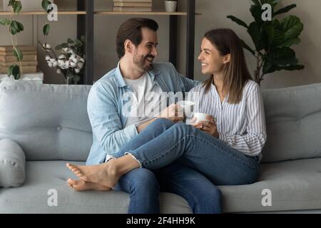 Happy couple relaxing on couch, holding cups, drinking hot beverages Stock Photo