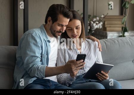 Close up young couple using gadgets together, sitting on couch Stock Photo