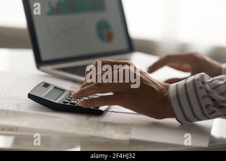 Close up businesswoman calculating company expenses, using laptop and calculator Stock Photo