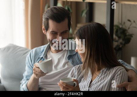 Close up happy young couple hugging, holding cups, drinking tea Stock Photo