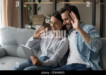 Close up smiling couple using tablet, waving hands, video call Stock Photo