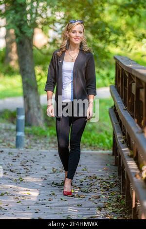 young positive, smiling, legant woman walks on a wooden footbridge on a sunny autumn day Stock Photo