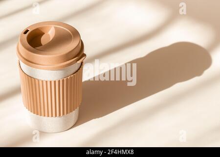 Reusable cup, biodegradable travel plastic coffee mug for take away. Sustainable bamboo eco friendly cup on natural shadow beige background. Zero Stock Photo