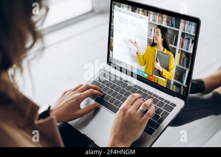 Distance learning by video conference. Female student uses video call app and a laptop for online learning from home, on the screen female teacher conducts an online lecture. E-learning concept Stock Photo