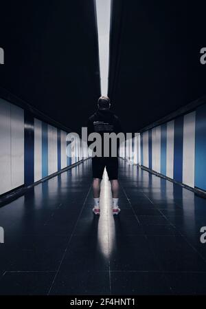 A man in sportswear standing in the middle of a long dark corridor with his back before the training Stock Photo