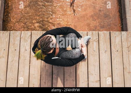 An overhead shot of a Spanish woman with colorful braided hair sitting on a wooden dock in a park Stock Photo