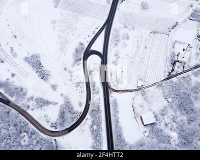 High angle top down aerial view drone image on road trough the trees and forest in mountain range covered with white snow in winter day near Knjazevac Stock Photo