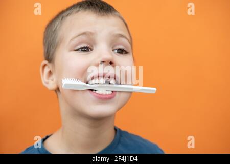 Boy without milk upper tooth in blue t-shirt holds toothbrush in his mouth on the orange background. Stock Photo