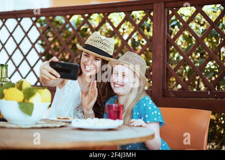 happy stylish family with plate of local farm lemons having video call on a smartphone and having breakfast in the terrace of guest house hotel. Stock Photo
