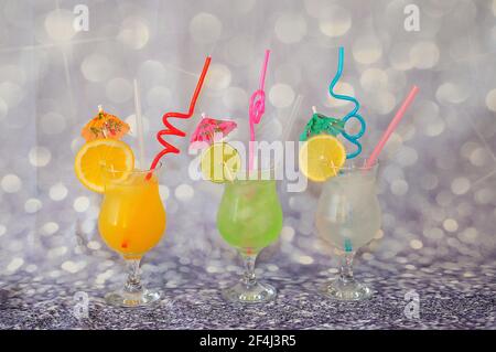 Three tall glasses with orange, lemon and lime juice on a gray background, decorated with citrus slices. Close-up. Stock Photo