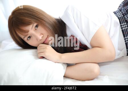 Portrait japanese school girl costume sleeping and smile in white tone bed room Stock Photo