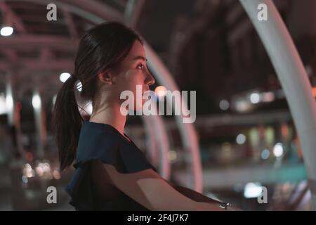 Depressed young Asian woman standing alone and lonely standing over footbridge looking away while thinking and daydreaming Stock Photo