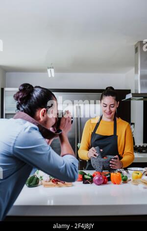 latin couple cooking mexican sauce and food taking photo in the kitchen in Mexico city Stock Photo