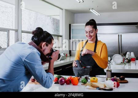 latin couple cooking mexican sauce and food taking photo in the kitchen in Mexico city Stock Photo