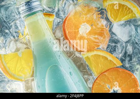 a bottle of green light green soda cocktail in cold water with ice cubes and pieces of oranges and fruit. Stock Photo