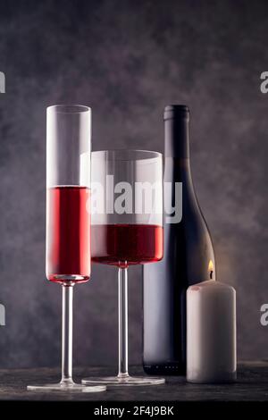 Wine glasses and a bottle of red wine on a gray background, still life with a burning candle. Stock Photo