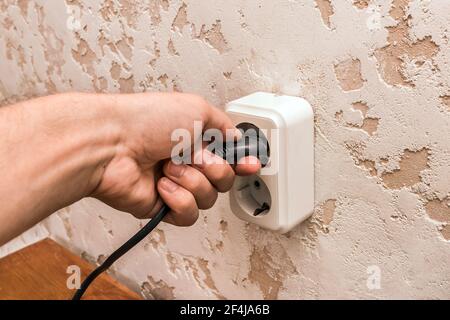 A man hand inserts or removes a plug from an outlet in a modern interior. Safe use of electrical appliances concept. Stock Photo