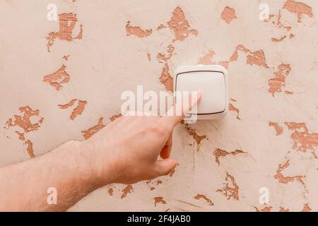 The guy's hand turns off the light with an electric switch in a modern room interior background. Stock Photo