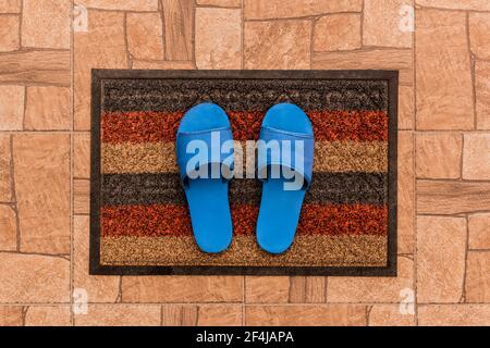 Men's blue house slippers stand on a foot mat on a brown tiled floor texture background, top view. Stock Photo