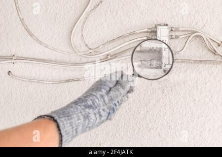 The hand of an industrial worker in a construction glove examines a large antenna splitter with a magnifying glass. Stock Photo