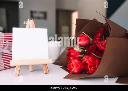 Red tulips bouquet, coffee cup, empty white frame, pink gift box, greeting card Stock Photo