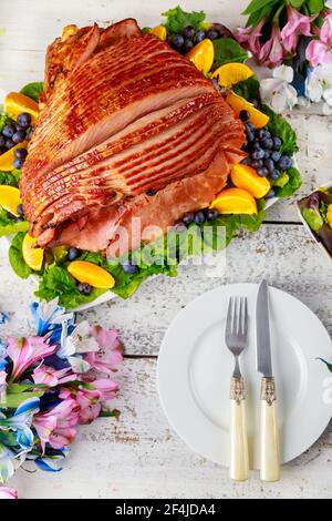 Delicious honey smoked pork ham with table set on wooden background. Stock Photo