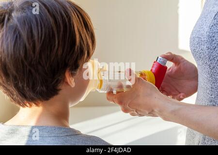 A caucasian woman is giving emergency asthma medication to a small kit during an attack. She uses aerosol chamber with valve mask to deliver bronchodi Stock Photo