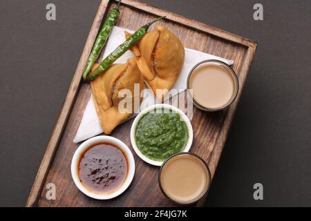 Indian snack Homemade spicy and delicious samosa served with green, tamarind chutney cutting masala tea, chai, Stock Photo