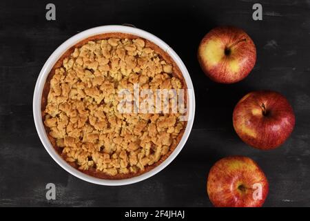 Top view of whole traditional European apple pie with topping crumbles in white springform pan on dark background Stock Photo