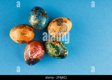 Five easter eggs painted in blue, green, red and yellow lie in a circle. Painted easter eggs on a blue background. Flat lay. Copy space. Close up . Stock Photo