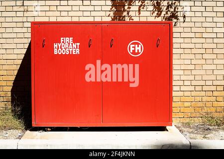Red fire hydrant booster cabinet against a brick wall on a sunny day Stock Photo