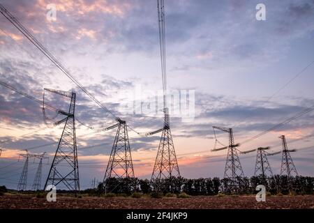 Electrical pylons and high voltage power lines at sunset background. Group silhouette of transmission towers. Stock Photo