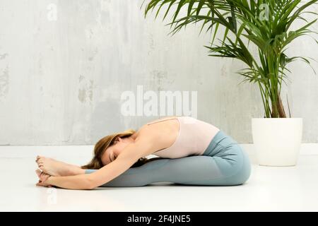 Woman doing a Pascimottanasana or Seated Forward Bend yoga pose for relaxation and to stretch her legs and spine with copyspace on a grey wall beyond Stock Photo