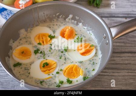 A pot with fresh boiled halved eggs in a delicious white herb sauce served isolated on a wooden kitchen table Stock Photo