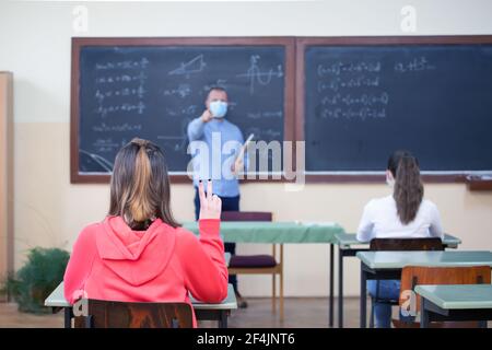 Teacher and his students wearing protective face mask in the classroom. Social distanting and classroom safety during coronavirus epidemic Stock Photo