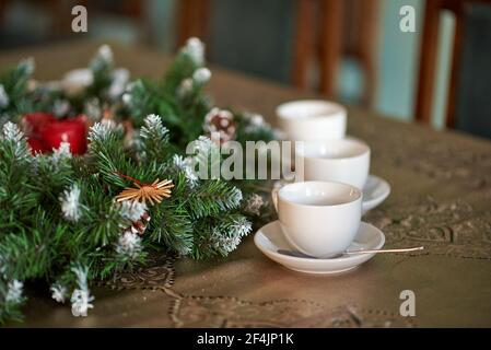 Three white tea cups with saucers and spoons near cones and spruce branches. Stock Photo