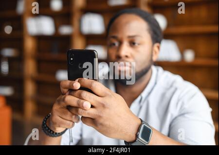 Suspicious man taking photo of criminal act or serious African American hodling mobile phone and typing text message, reading bad news, young upset black guy looking at the cellphone screen Stock Photo