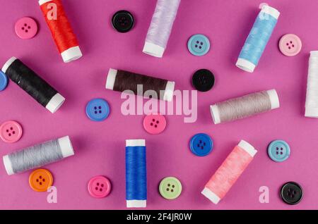 Multicolored thread spools and buttons on purple background. A set of thread. Ten spools. Random buttons. Top view, flatlay. Stock Photo
