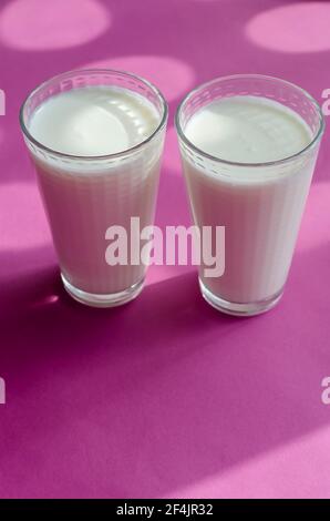 Two full glasses of kefir on a pinky surface with shadows. Transparent glasses with a checkered pattern. Abstract sunny shadows on pink. Selective foc Stock Photo