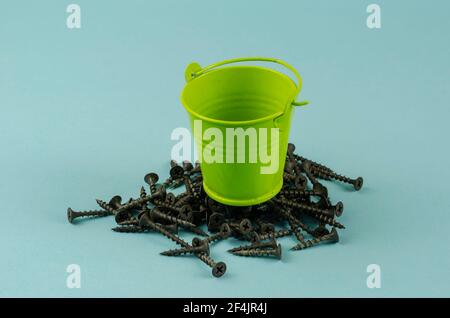Screws and a small green bucket on a blue background. Empty bucket on top with metal fasteners. Close-up, selective focus. Stock Photo