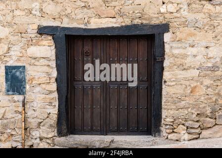 Old wooden door in stone wall in traditional house in the village of Horcajuelo de la Sierra in Madrid Stock Photo