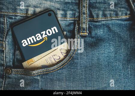 Smartphone with Amazon app logo with british pounds cash in blue jeans pocket Stock Photo